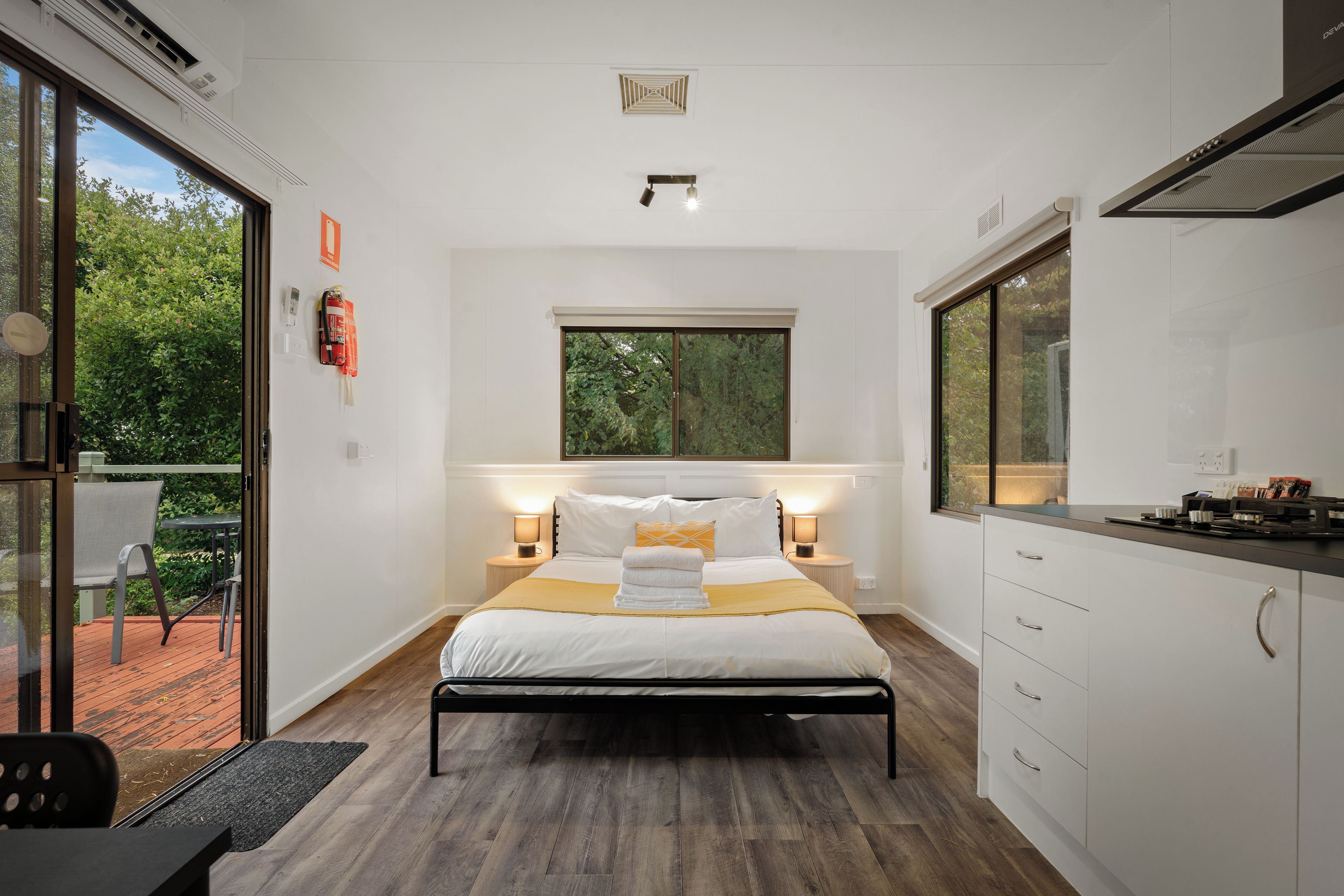A modern bedroom with a bed, bedside lamps, a window, and a view of greenery.