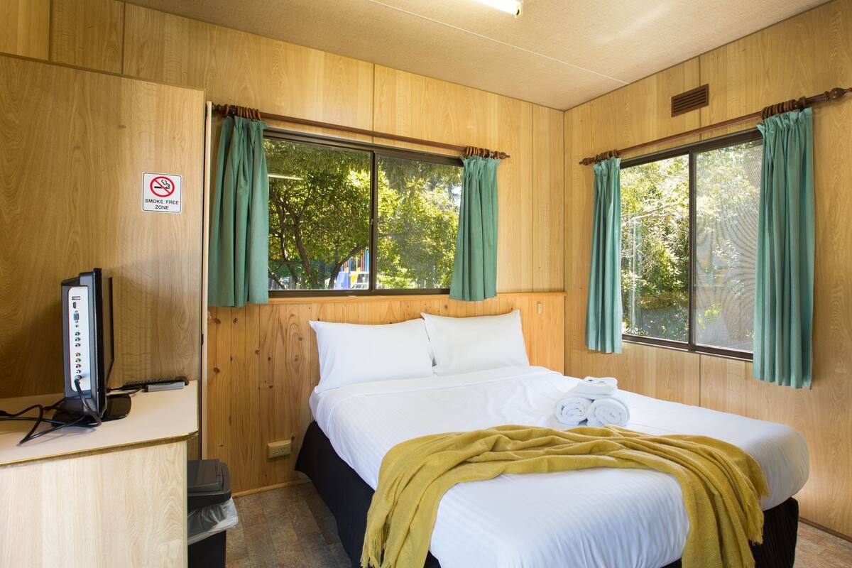 A room with a bed, a desk with a computer, and two windows with curtains.