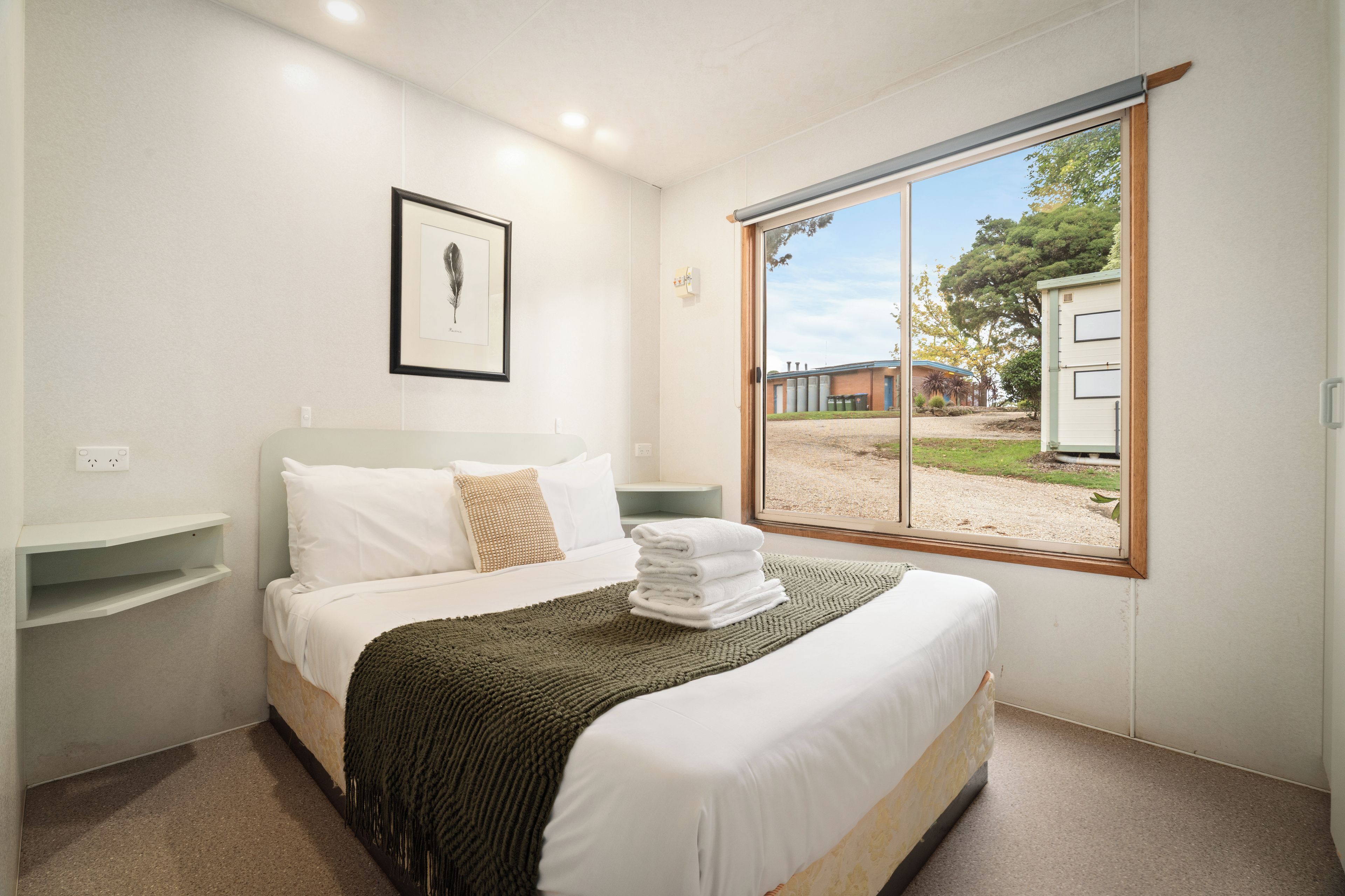 A hotel room with a bed, a framed picture on the wall, and a window with a view of the outside.