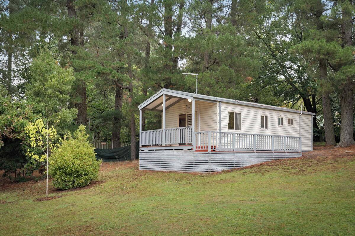 A single-story mobile home with a covered porch, surrounded by trees.