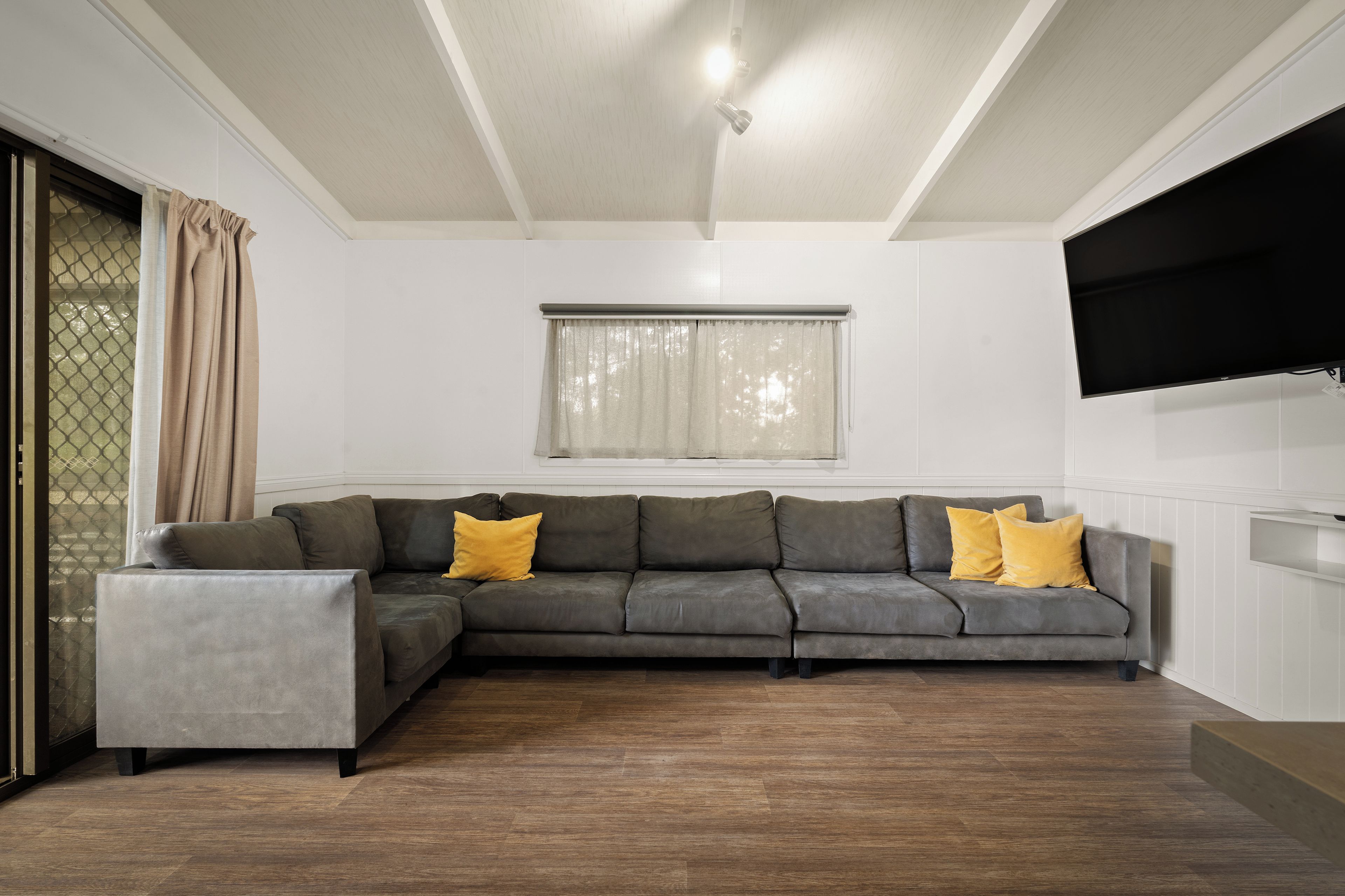 A modern living room with a sectional sofa, a small side table, and a flat-screen TV mounted on the wall.