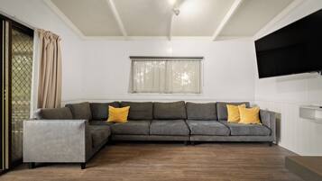 A modern living room with a sectional sofa, a small side table, and a flat-screen TV mounted on the wall.