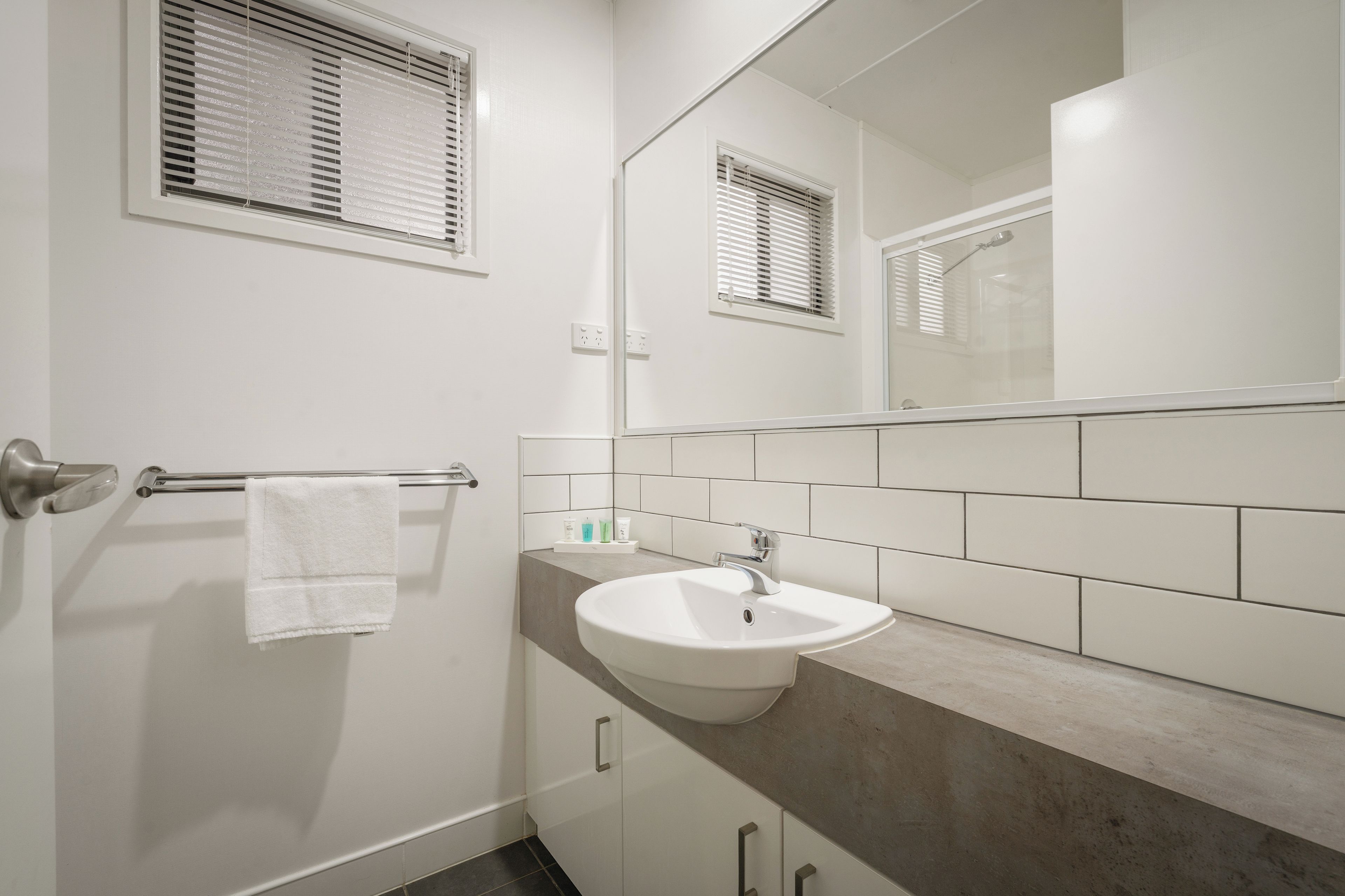 A bathroom with a white sink, a towel rack, a mirror, and a window with blinds.