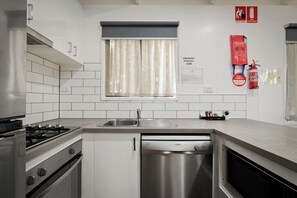 Een moderne keuken met witte tegels, roestvrijstalen apparatuur, een raam met gordijnen en brandveiligheidsmiddelen.