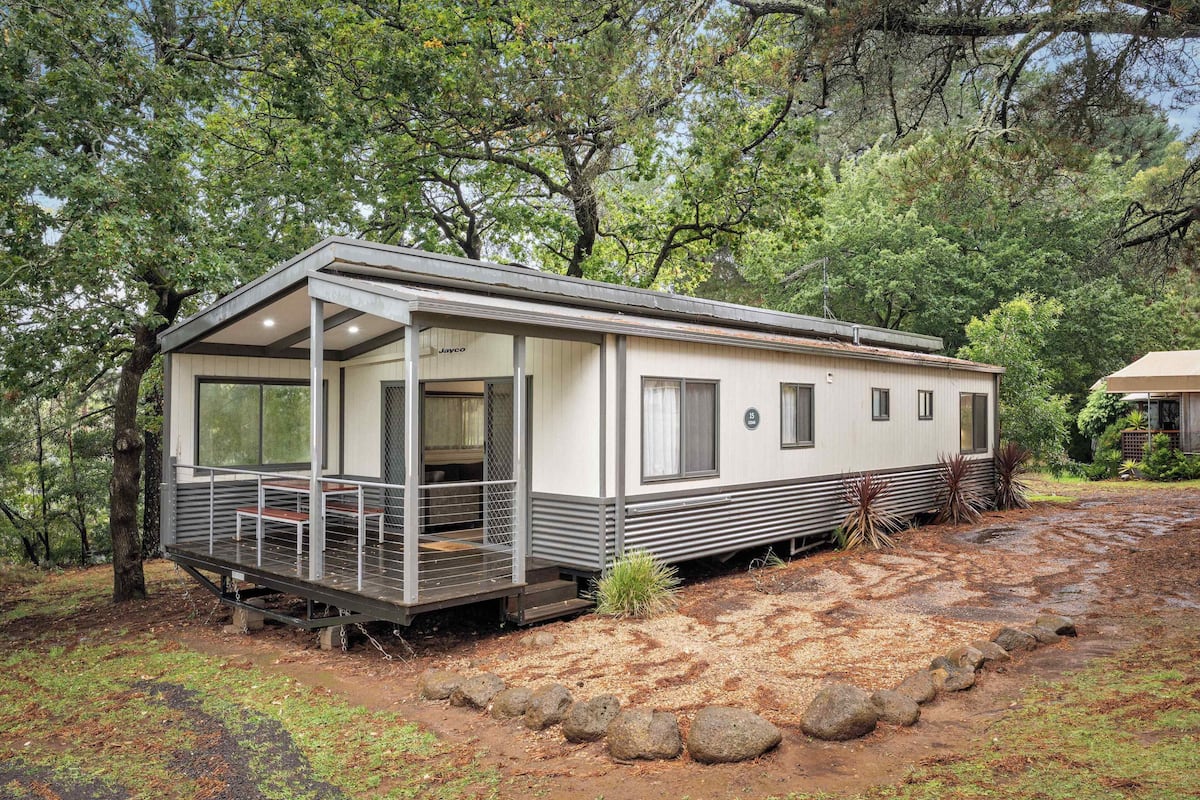 A mobile home with a porch, large windows, and a covered outdoor area.