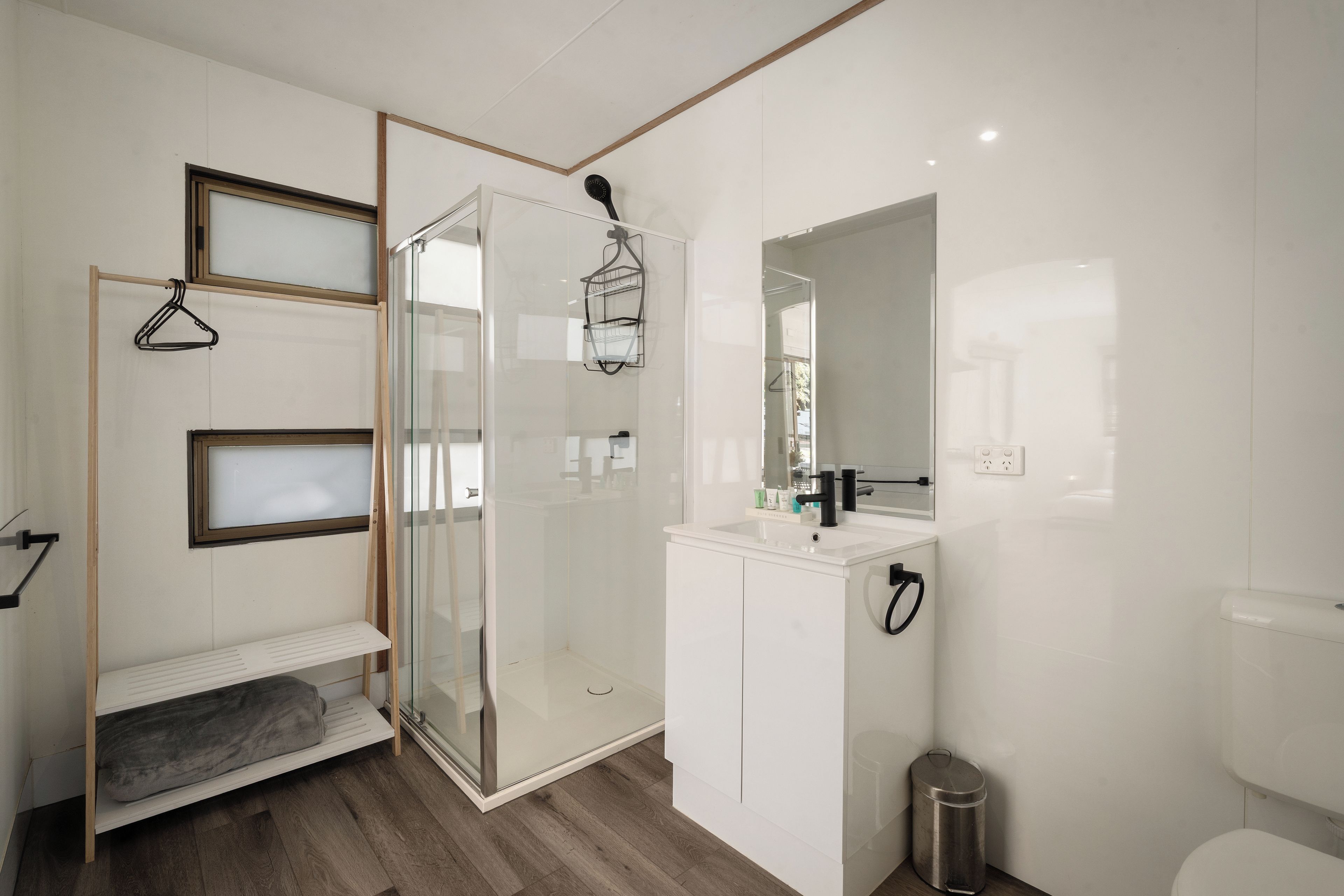 A modern bathroom with a glass shower enclosure, a white vanity with a mirror, and a wooden bench.
