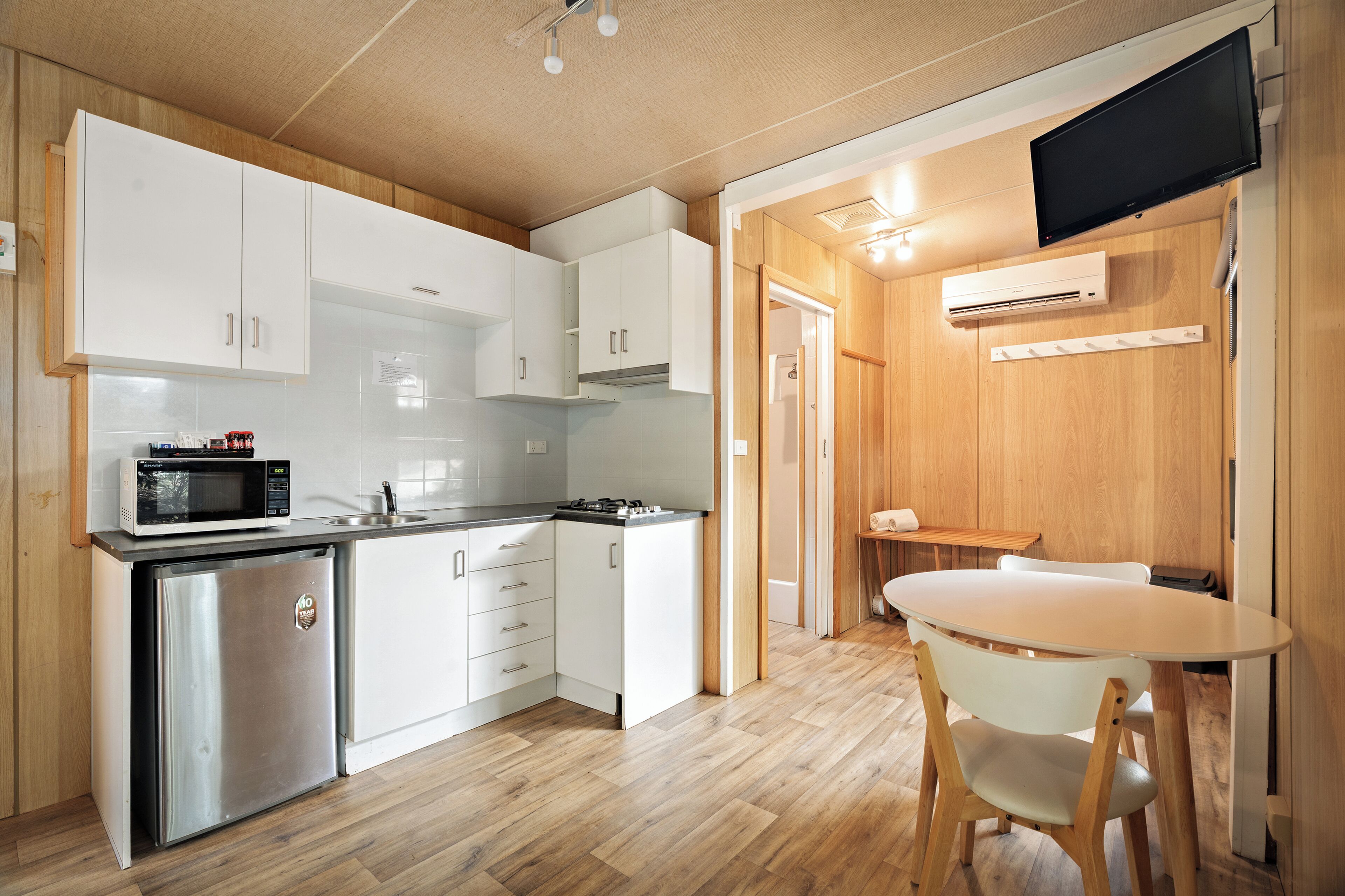 Cocina compacta con gabinetes blancos, microondas, refrigerador pequeño, estufa a gas y una mesa de madera con sillas.