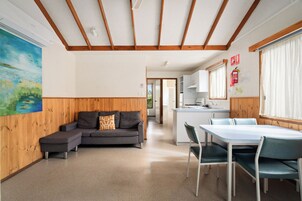 Un interior moderno con techo de madera, un sofá gris, una mesa de comedor con sillas y una zona de cocina.