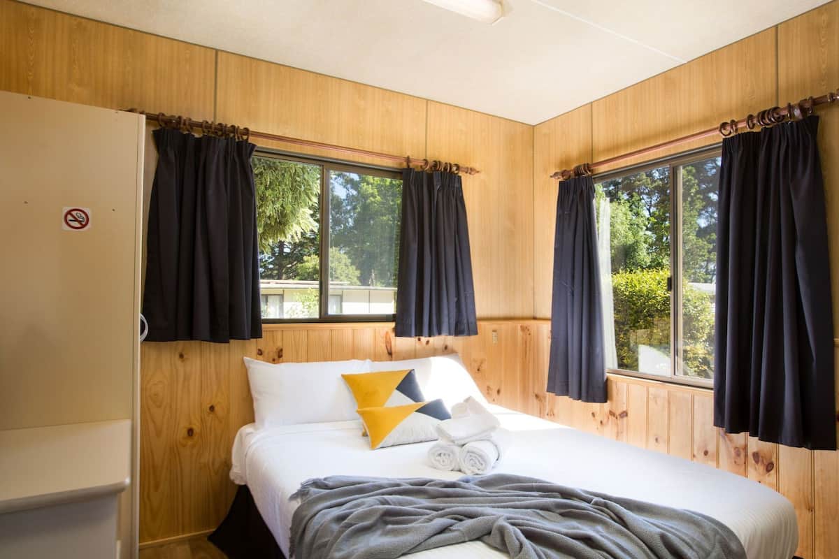 A room with a bed, wooden walls, and windows with curtains.