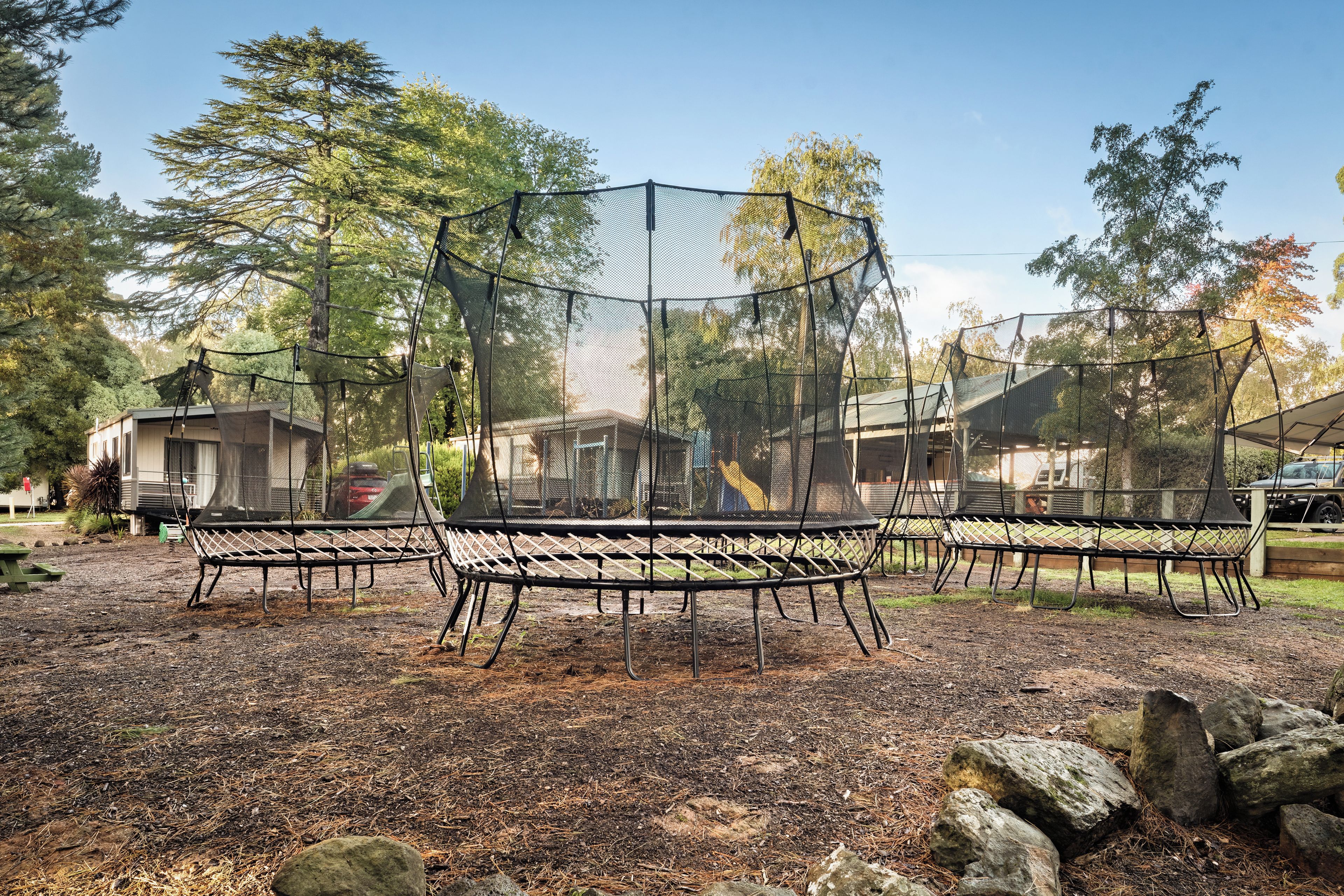 Un parque infantil con red de seguridad, rodeado de árboles y suelo de tierra.