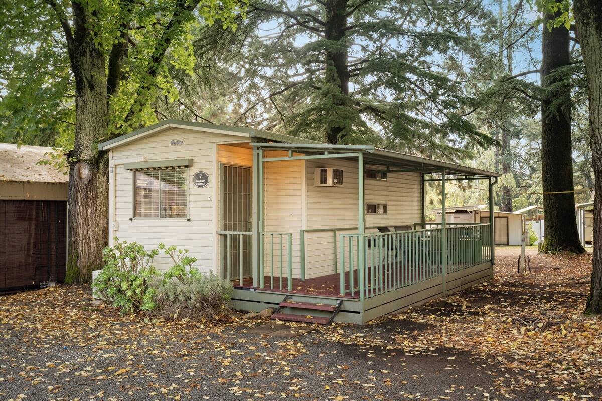 A small, single-story cabin with a porch, surrounded by trees.