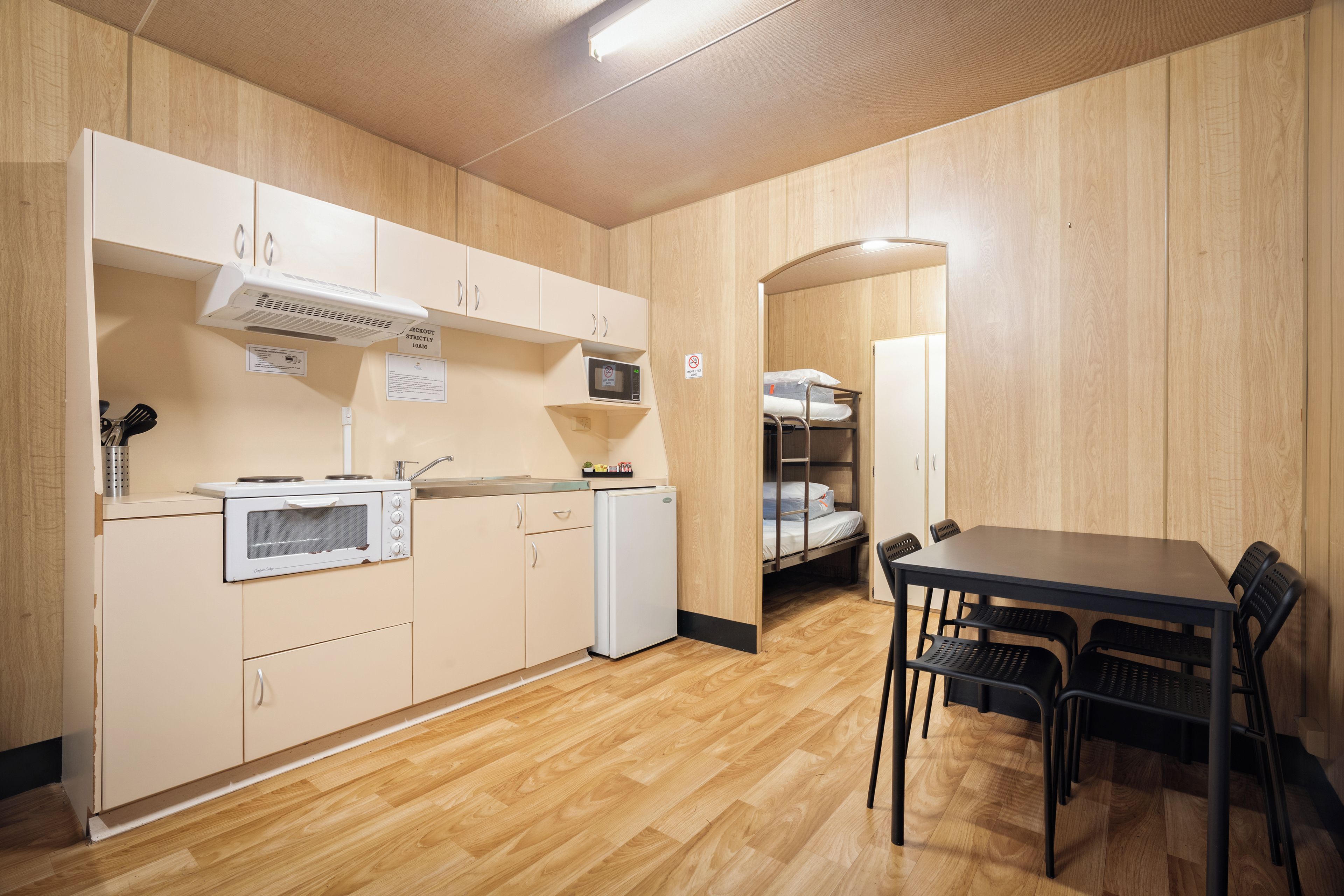 Cocina compacta con microondas, estufa y lavabo, un refrigerador pequeño y un comedor con mesa y sillas.