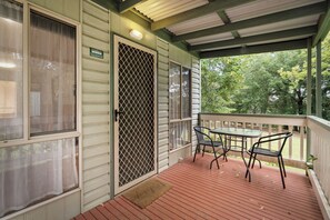 Une véranda abritée avec une table et des chaises, une porte moustiquaire et une vue sur les arbres.