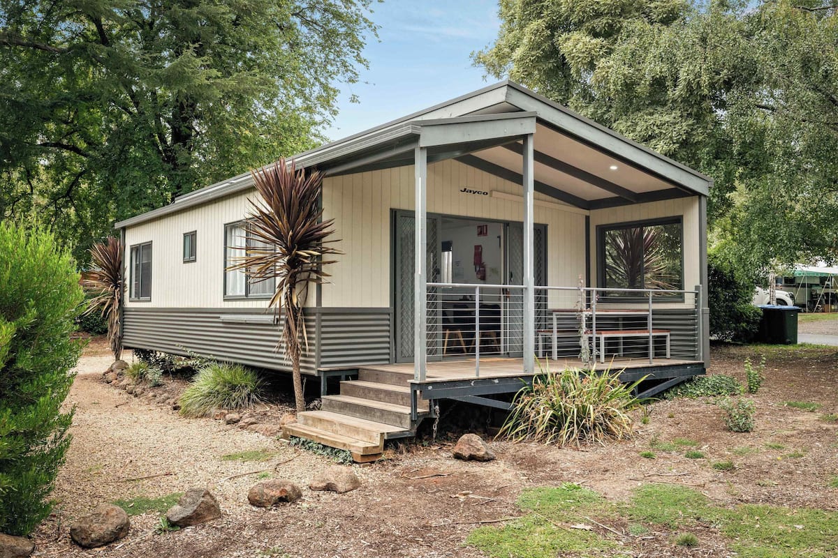 A single-story mobile home with a covered porch, a small front entrance, and a visible fire extinguisher.