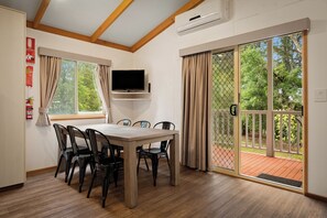 Un comedor con mesa y sillas, un televisor montado y un gran ventanal corredizo que da a una terraza exterior.