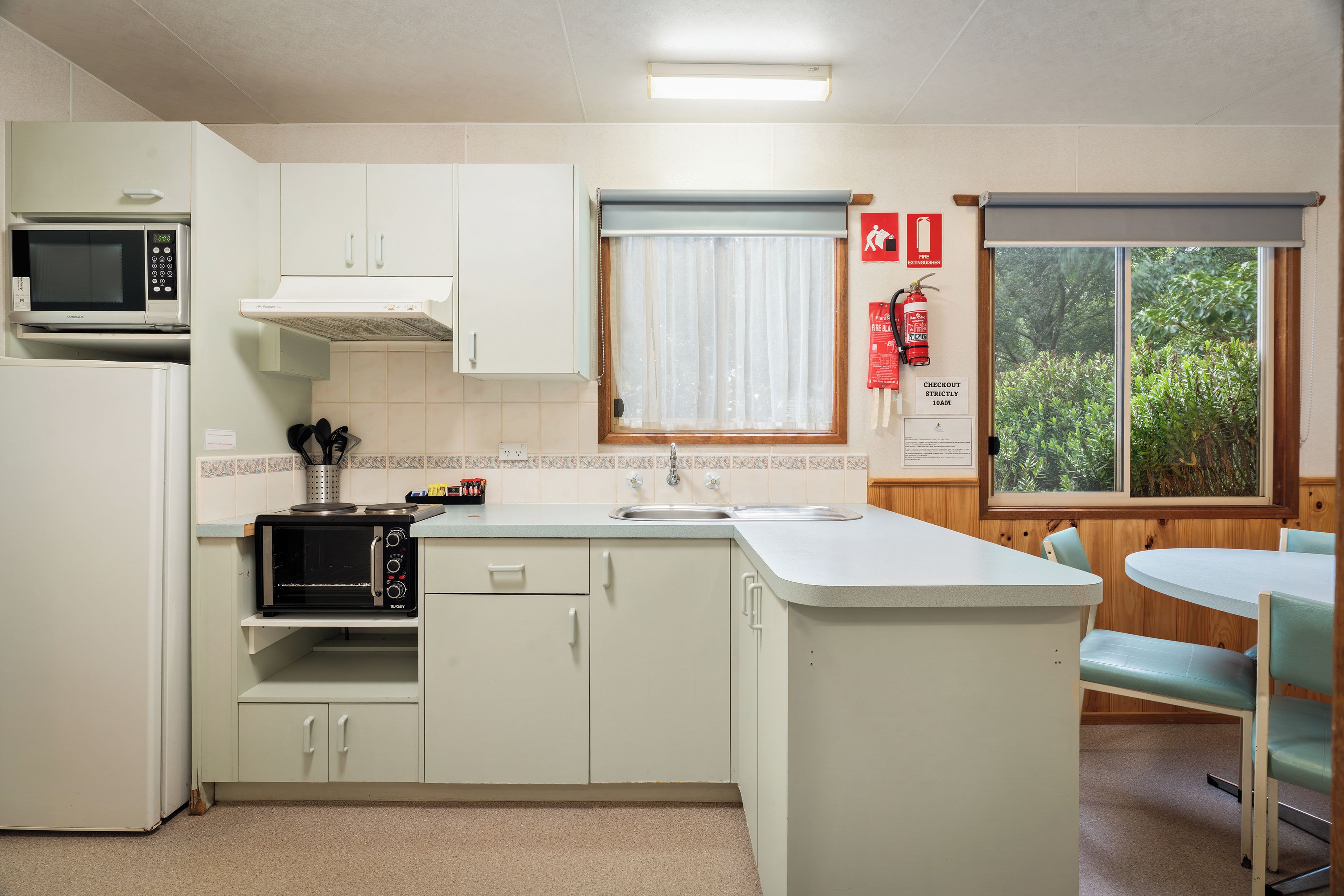 A compact kitchen with a microwave, toaster, and sink. There is a window with a view of greenery outside.