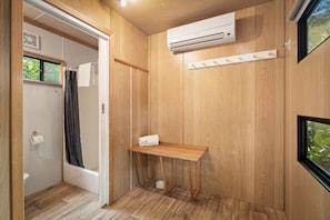 A bathroom with a wooden floor, a shower, a towel rack, and an air conditioning unit.