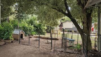 A fenced outdoor area with a doghouse, a bench, and a tree.