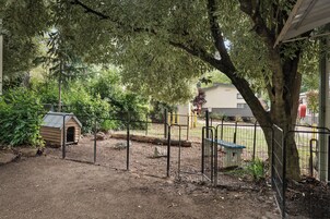 Un espacio exterior cercado con una caseta para perros, un banco y un árbol.