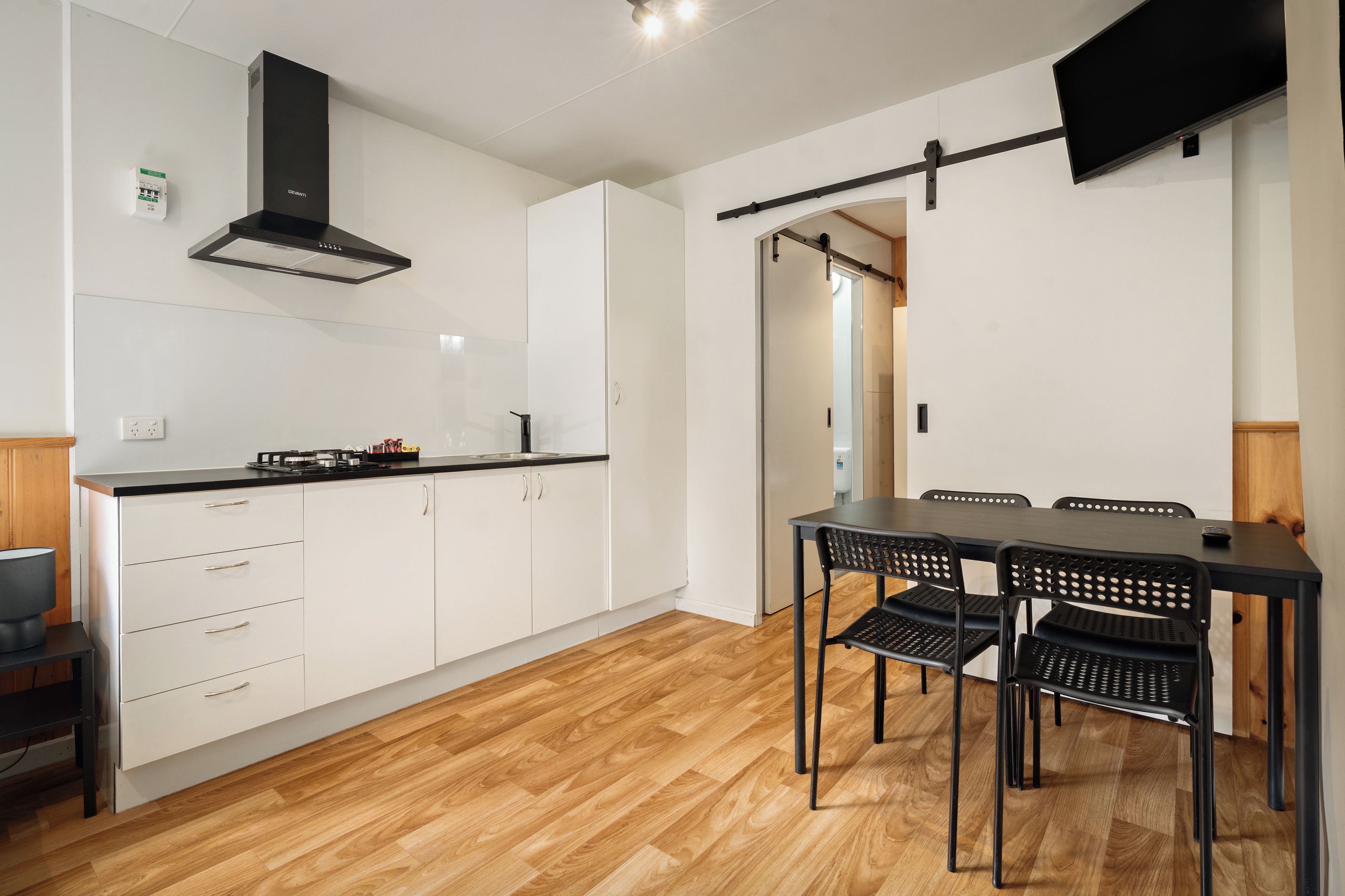Una cucina moderna con mobili bianchi, una cappa aspirante nera e un'area pranzo con tavolo e sedie neri.