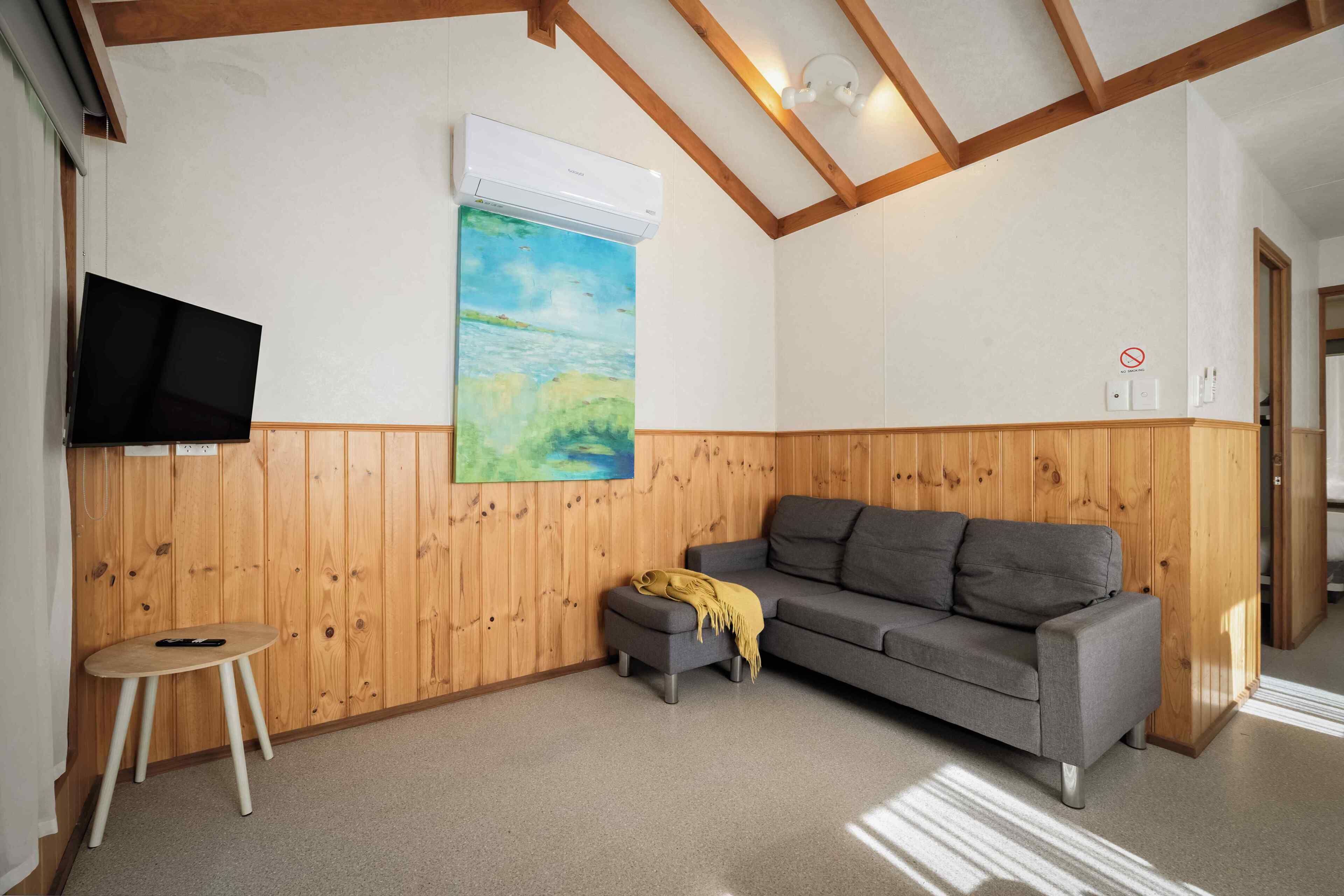 A room with a wooden wall, a gray sofa, a small table, and a painting.
