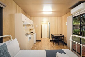 Een kleine kamer met een bed, kitchenette, eethoek en een raam.