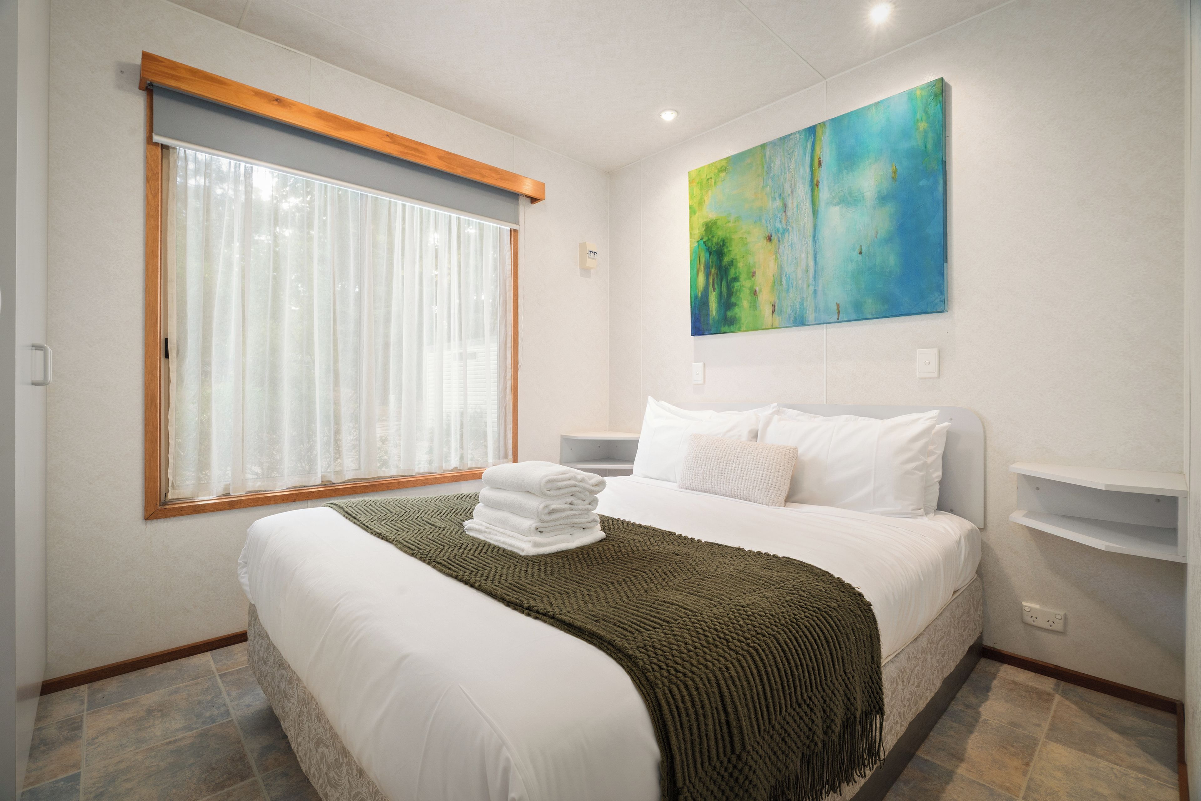 Quarto de hotel com cama, janela com cortinas, quadro na parede e mesa de cabeceira.