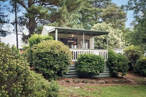 Une cabane dotée d’une véranda, entourée d’une végétation luxuriante et d’arbres.