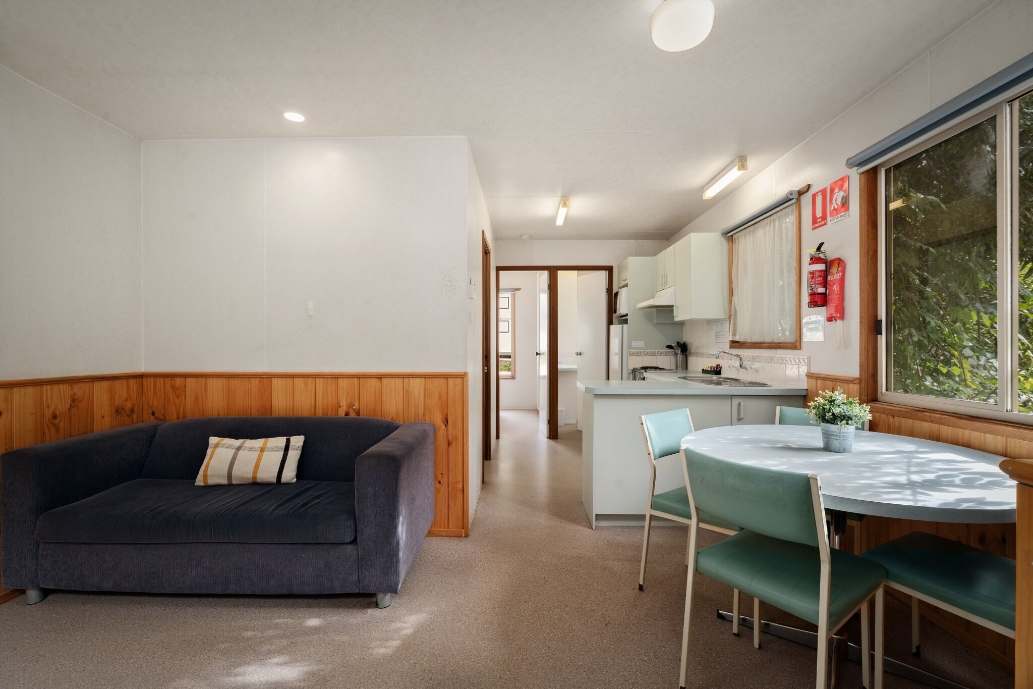 A room with a sofa, a dining table with chairs, a kitchen area, and a window with a view.