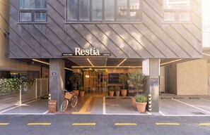 A hotel entrance with a modern facade, a bicycle parked outside, and potted plants. - Restia Hotel Suwon Station (Suwon)