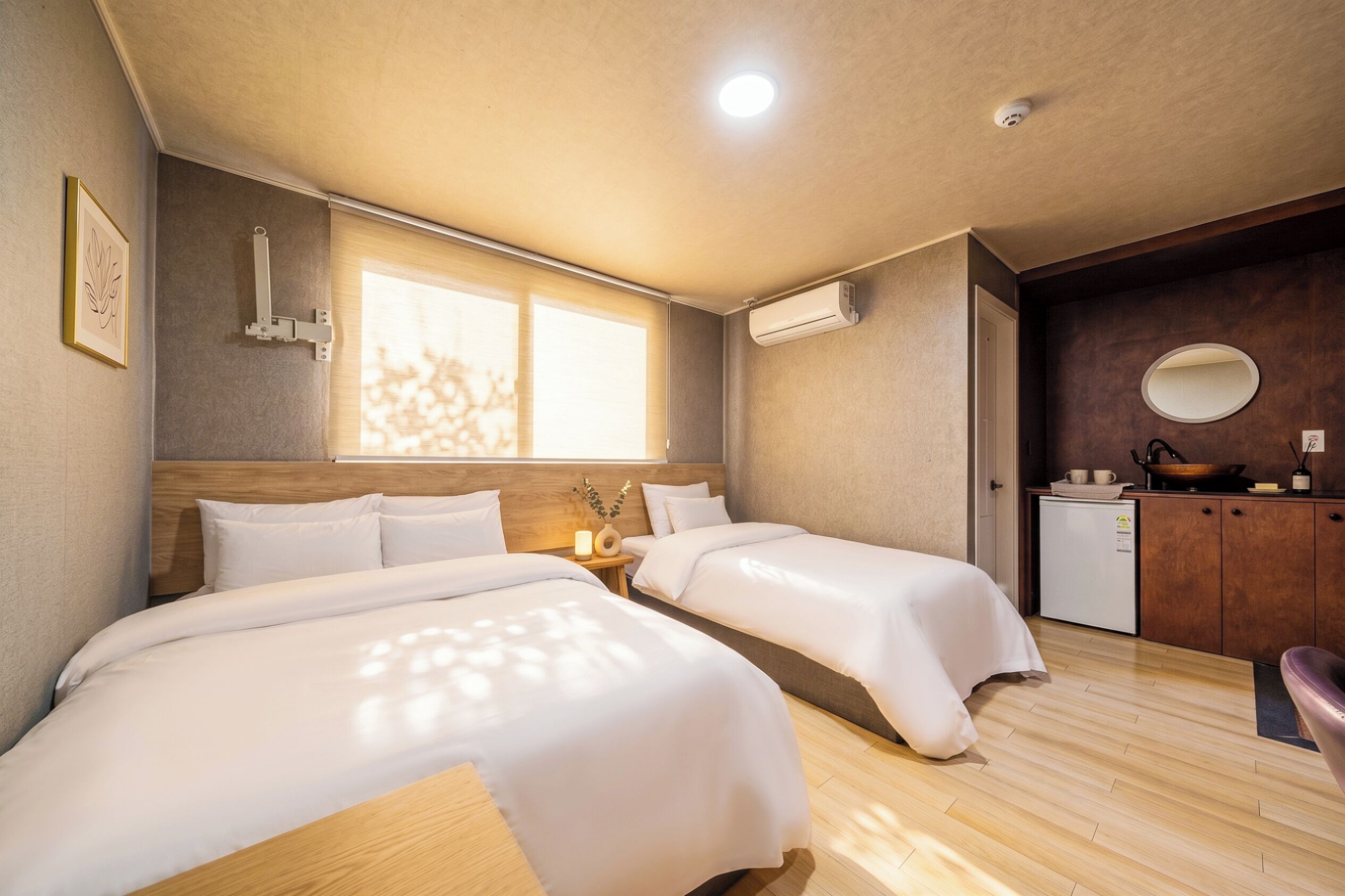 Une chambre d’hôtel avec deux lits, une petite kitchenette, une fenêtre et un luminaire au plafond.