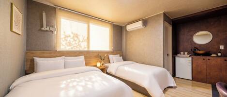 A hotel room with two beds, a small kitchenette, a window, and a ceiling light.