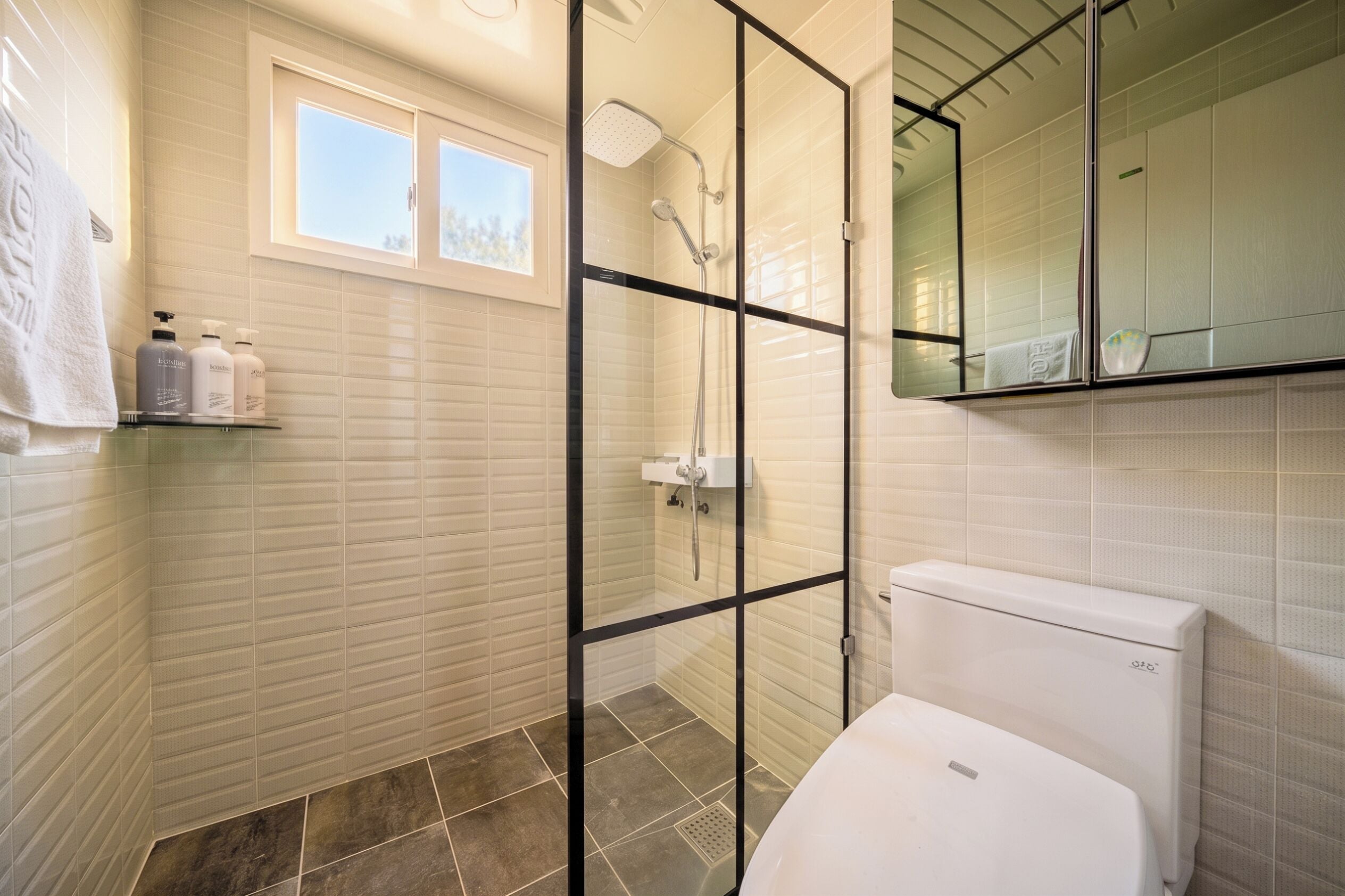 A modern bathroom with a glass-enclosed shower, a toilet, and a window.