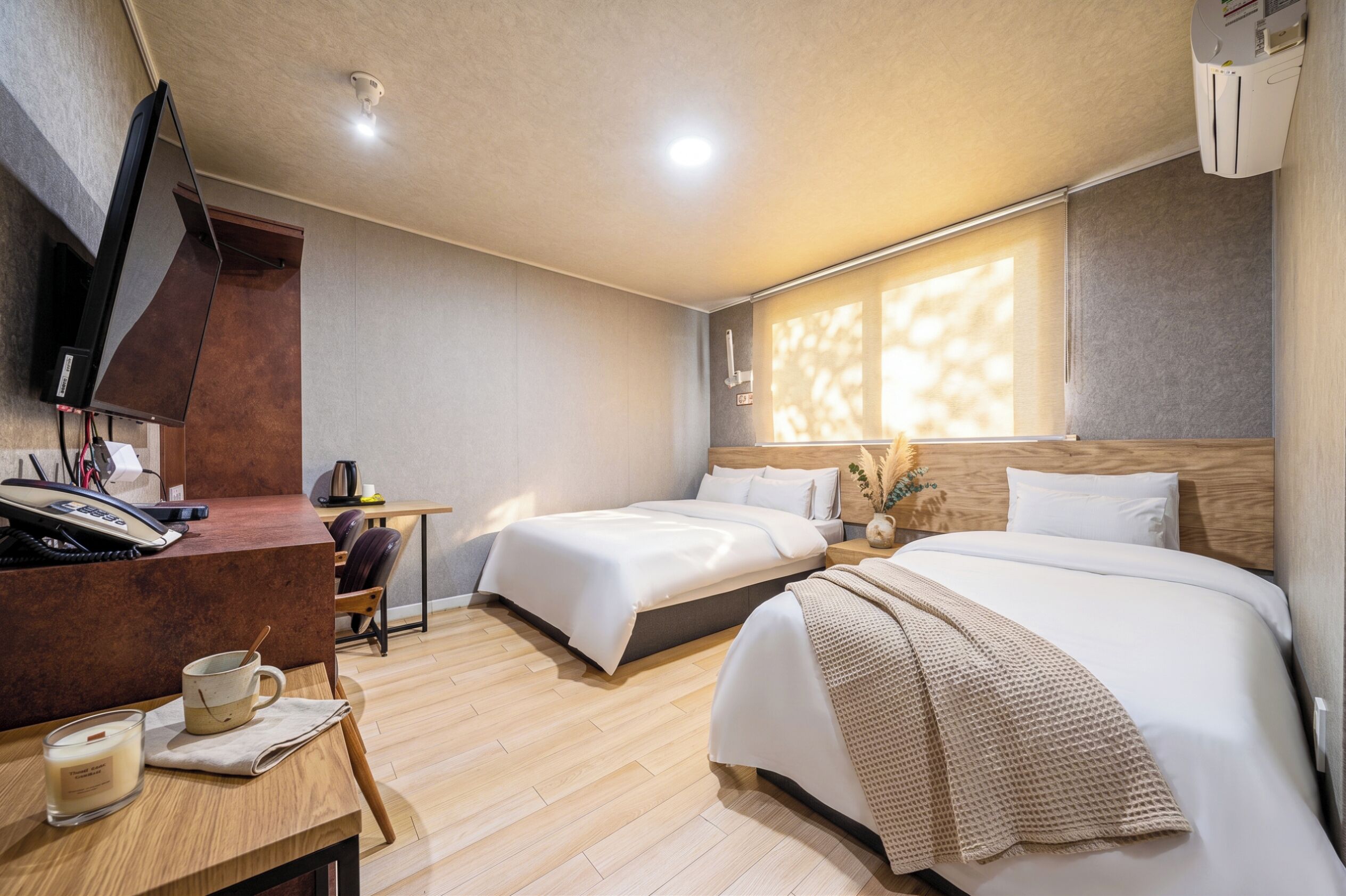 A hotel room with two beds, a desk with a phone, a coffee maker, and a window with natural light.