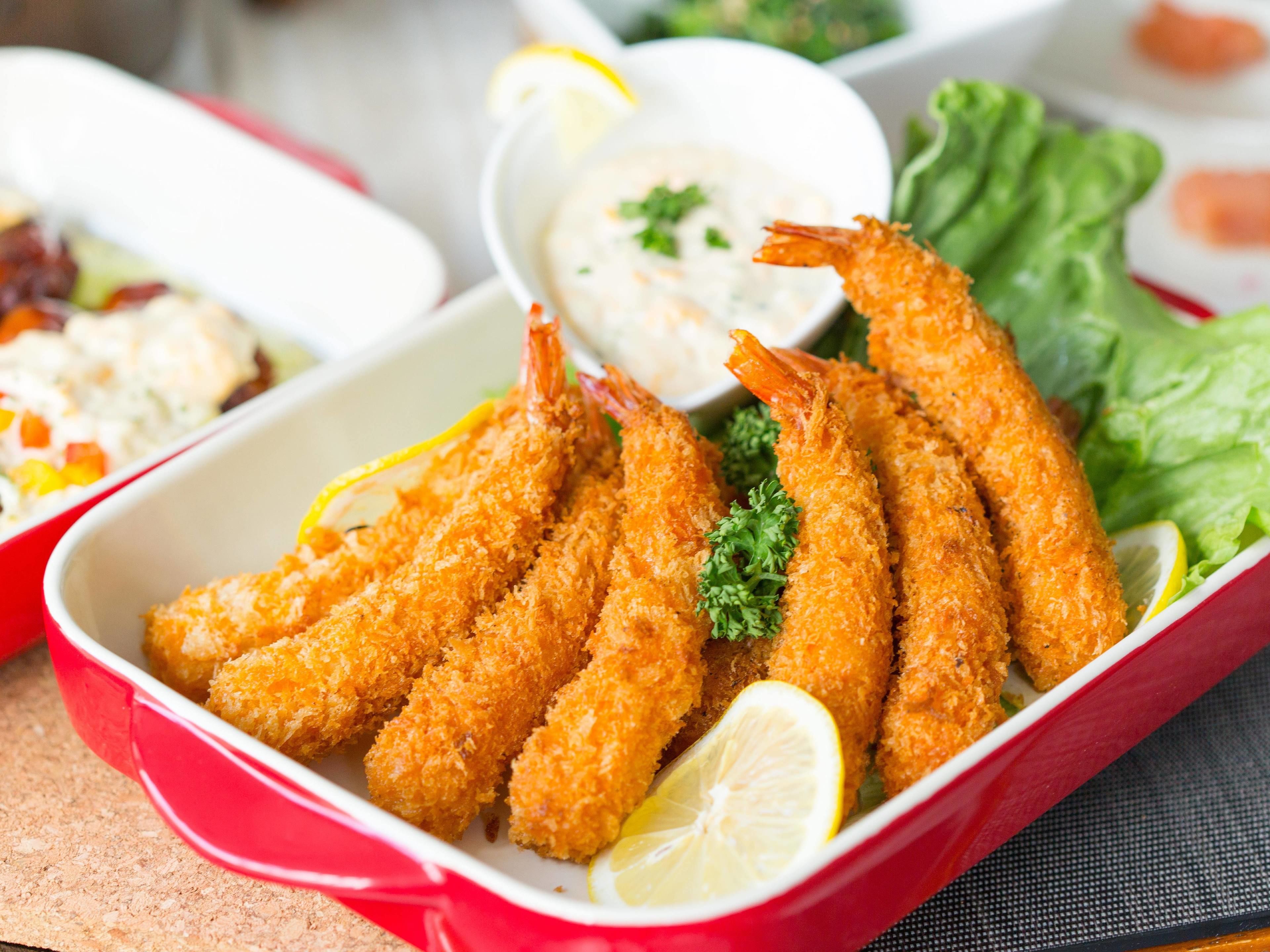 A dish of breaded and fried shrimp served with lemon wedges and a side of dipping sauce.