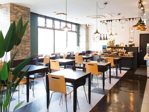 A modern dining area with tables and chairs, a kitchen counter with food, and large windows.