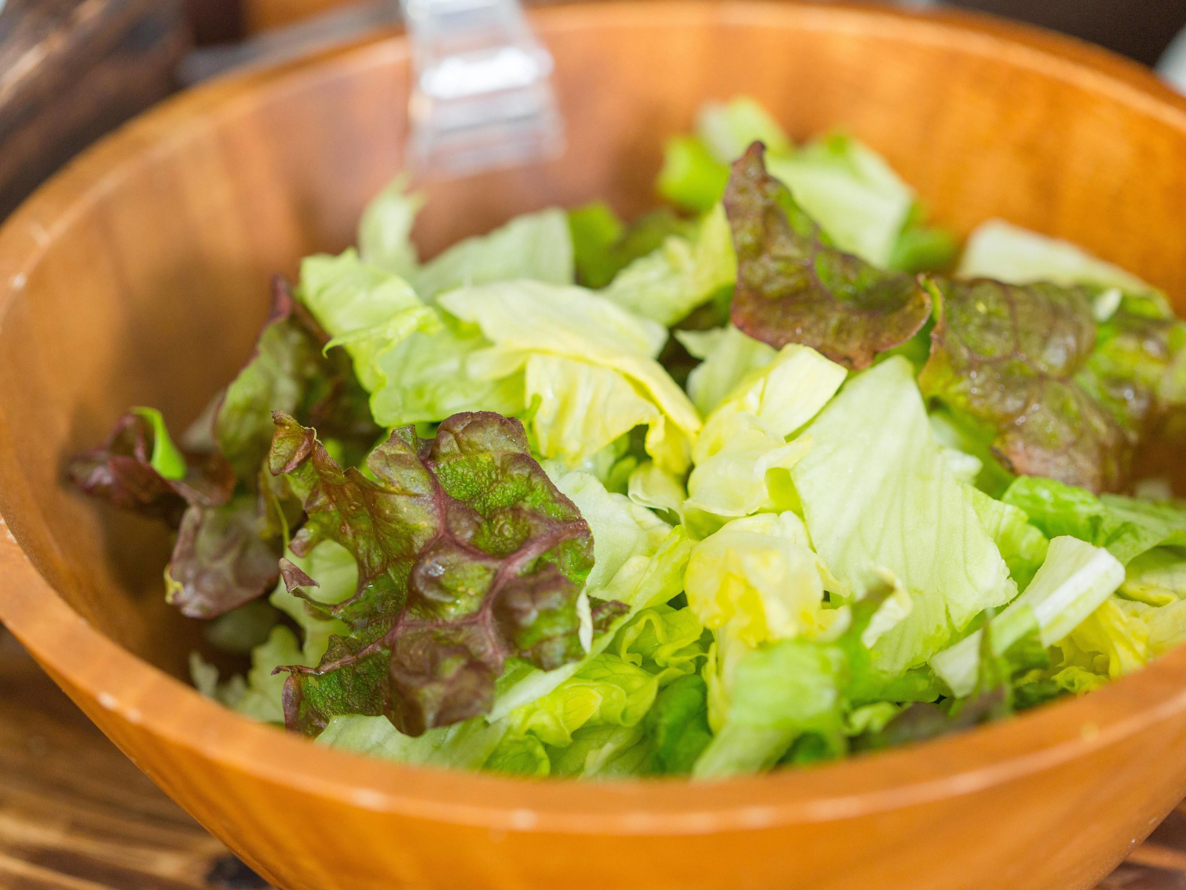 A wooden bowl containing a salad with mixed green and purple leaves.