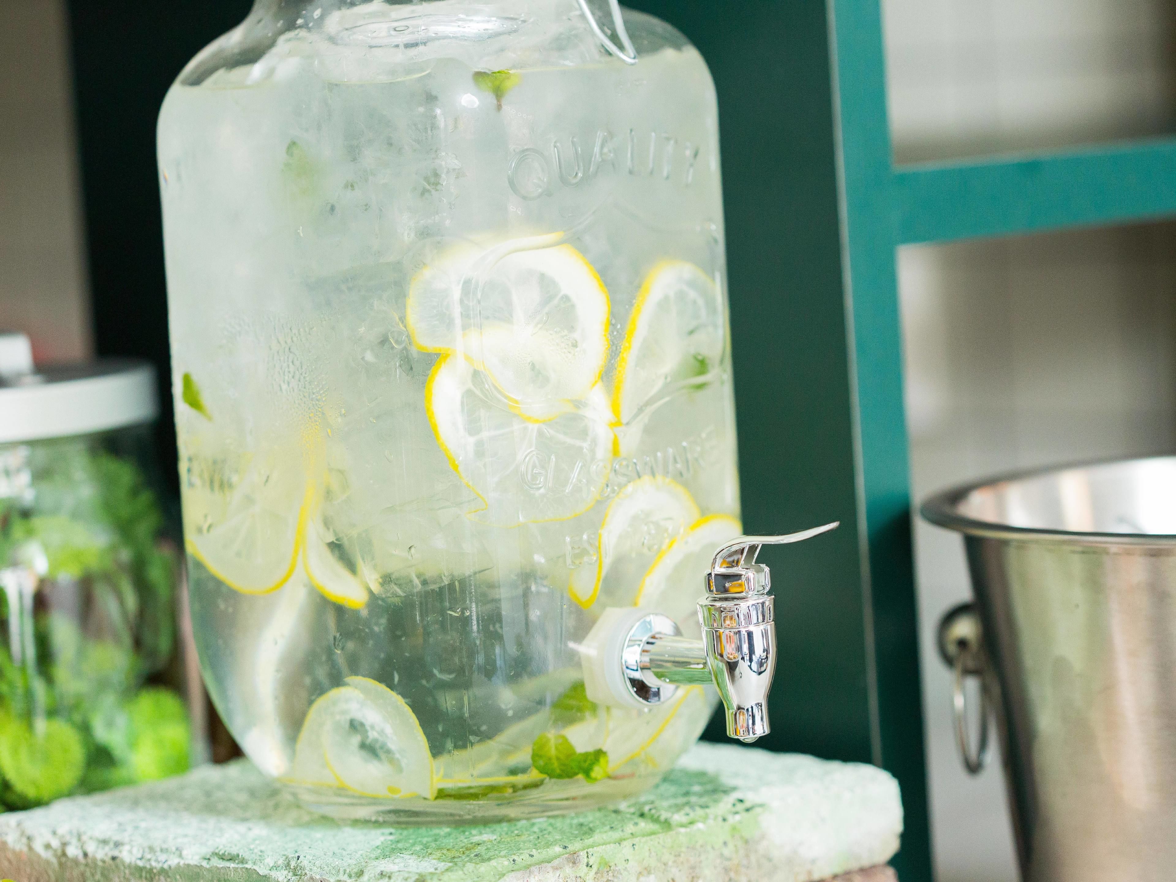 A large glass container with a tap, filled with water and lemon slices, placed on a surface.