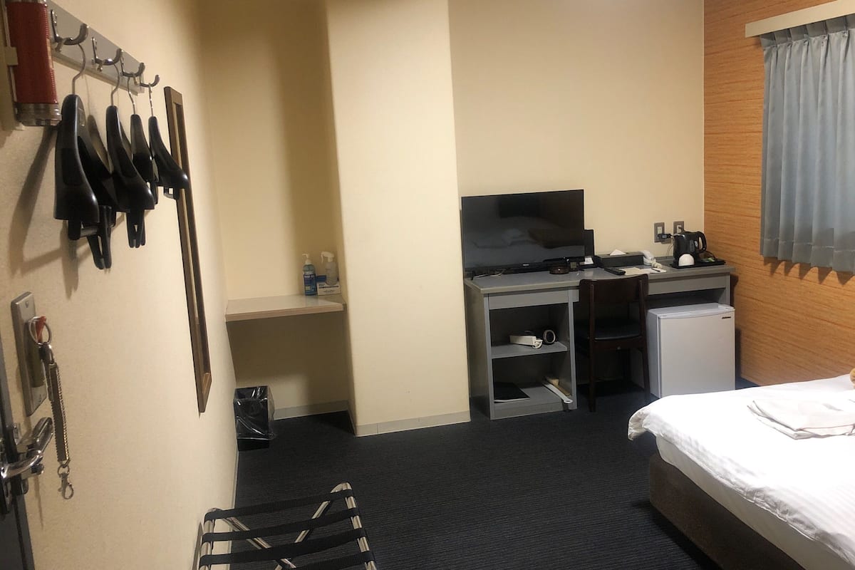 Habitación de hotel con cama, escritorio con computadora, televisor y refrigerador pequeño.