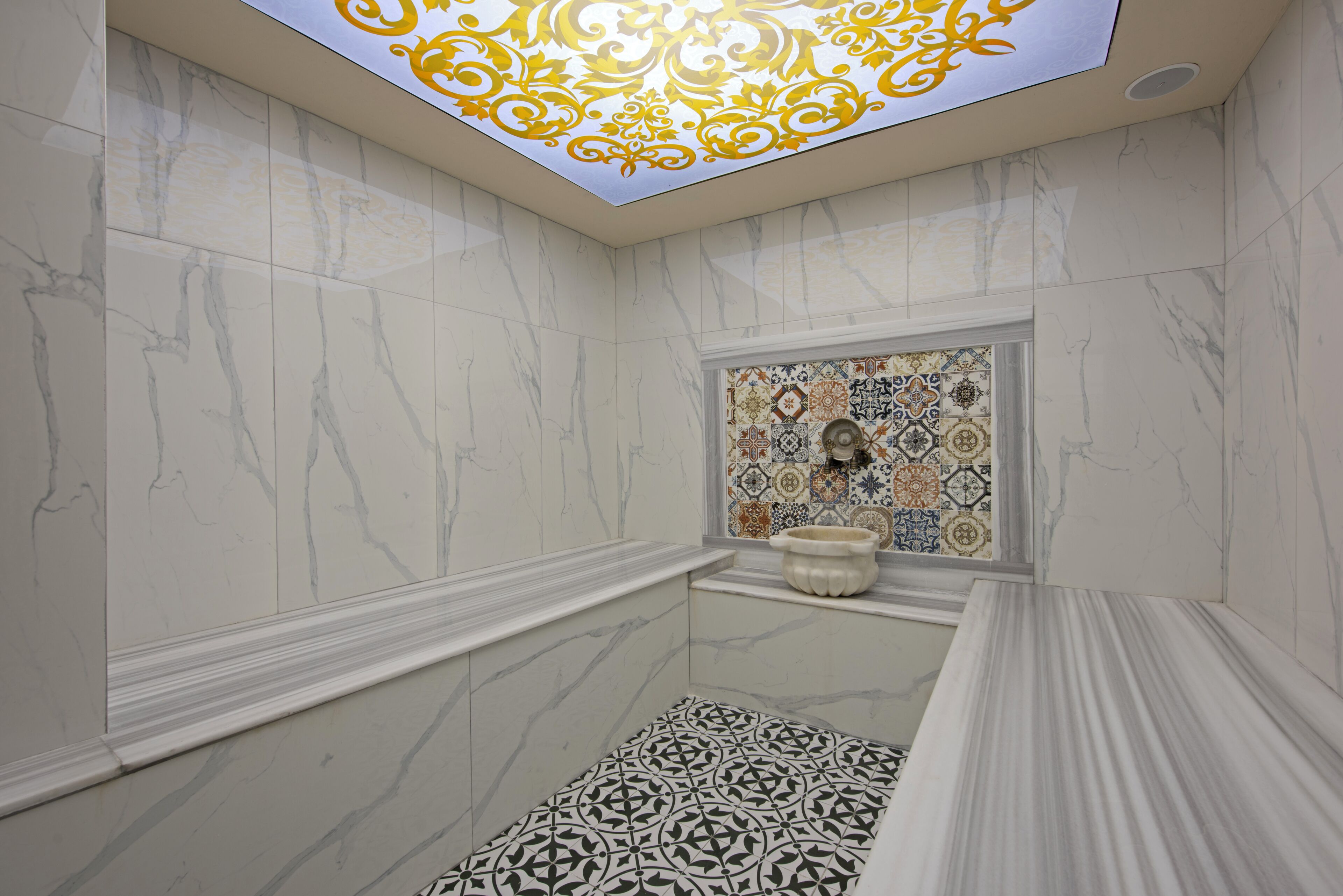 Un baño con paredes de mármol, piso estampado y techo decorativo.