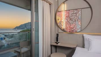 A hotel room with a balcony, a bed, a desk, and a wall art piece.