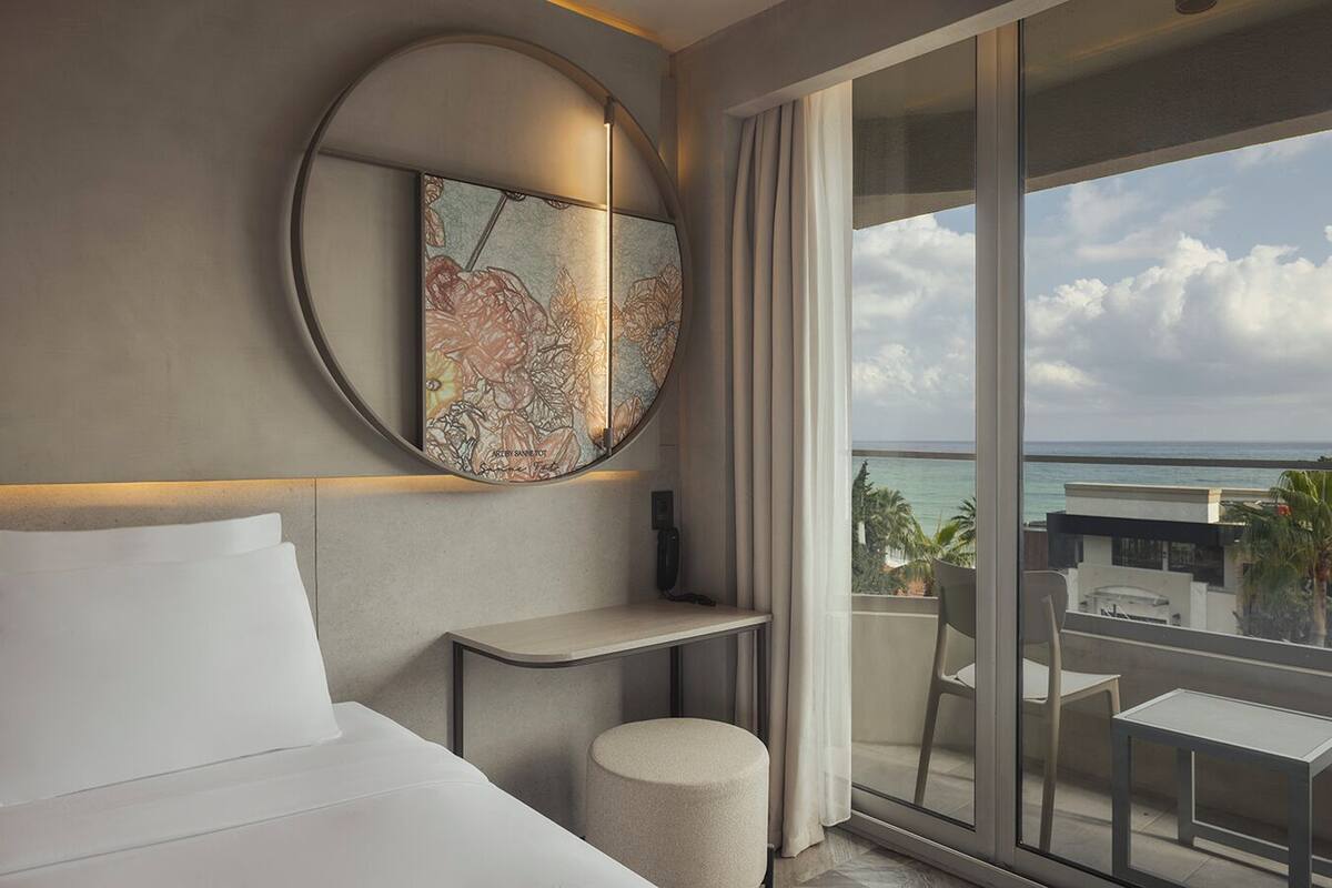 Een moderne hotelkamer met een groot bed, een ronde decoratie aan de muur, een klein tafeltje, een stoel en een balkon met uitzicht op de oceaan.