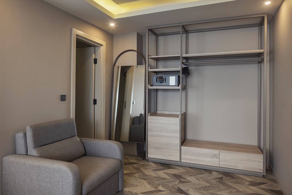Een moderne kamer met een grijze bank, een inloopkast met planken, een spiegel en een kleine radio.