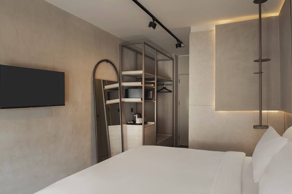 Een moderne hotelkamer met een bed, een aan de muur bevestigde televisie en een inbouwkast met planken.