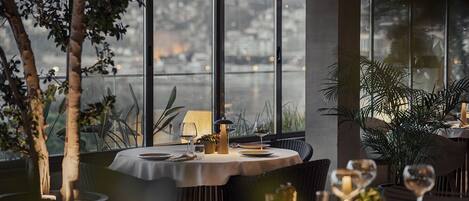 A restaurant with round tables, candles, and wine glasses.
