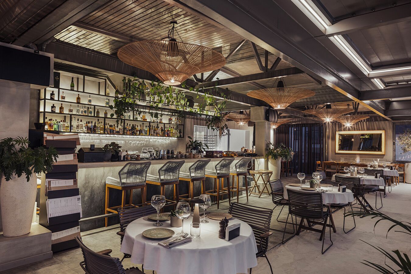 Un espace bar moderne, avec un assortiment de bouteilles d’alcool, des lampes suspendues en osier et un comptoir de bar.