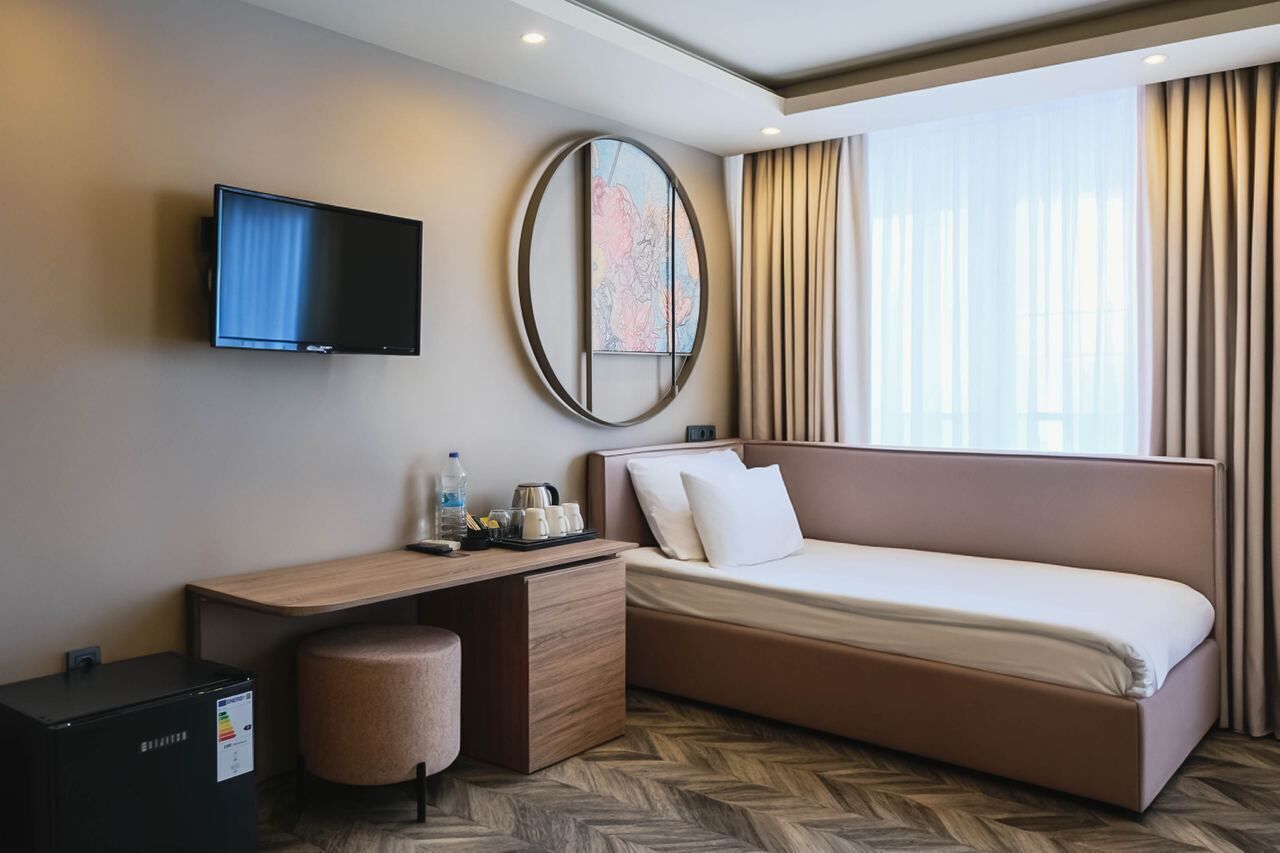 Ein modernes Hotelzimmer mit Flachbildfernseher, einem runden Spiegel, einem Bett, einem Schreibtisch und einem Couchtisch.