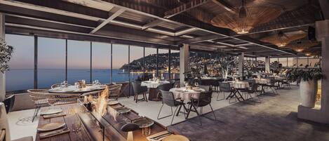 Restaurante con terraza al aire libre y vistas al mar, con amplios ventanales y una decoración interior moderna.