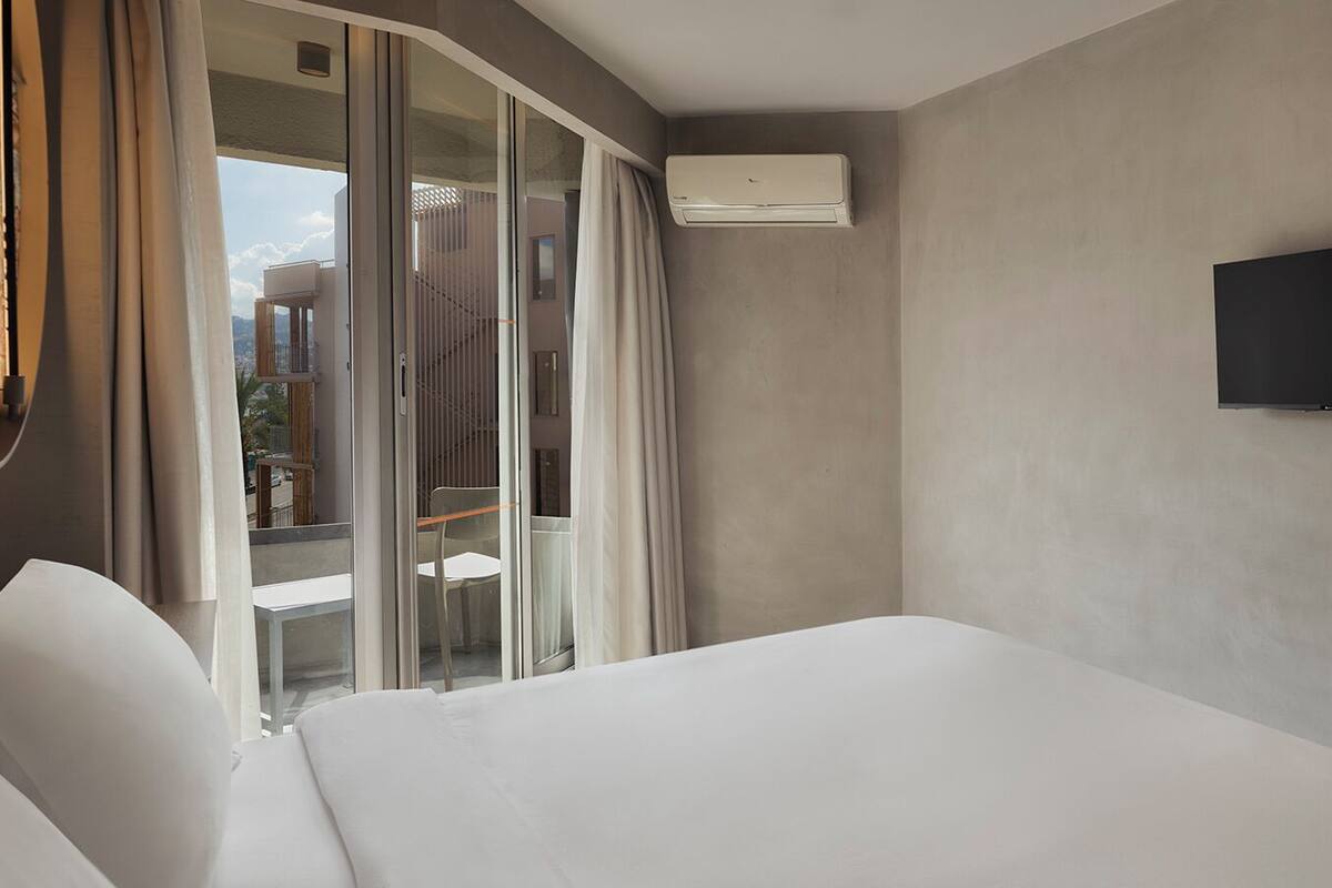 Een hotelkamer met een groot bed, een flatscreen televisie aan de muur en een schuifglazen deur naar een balkon.