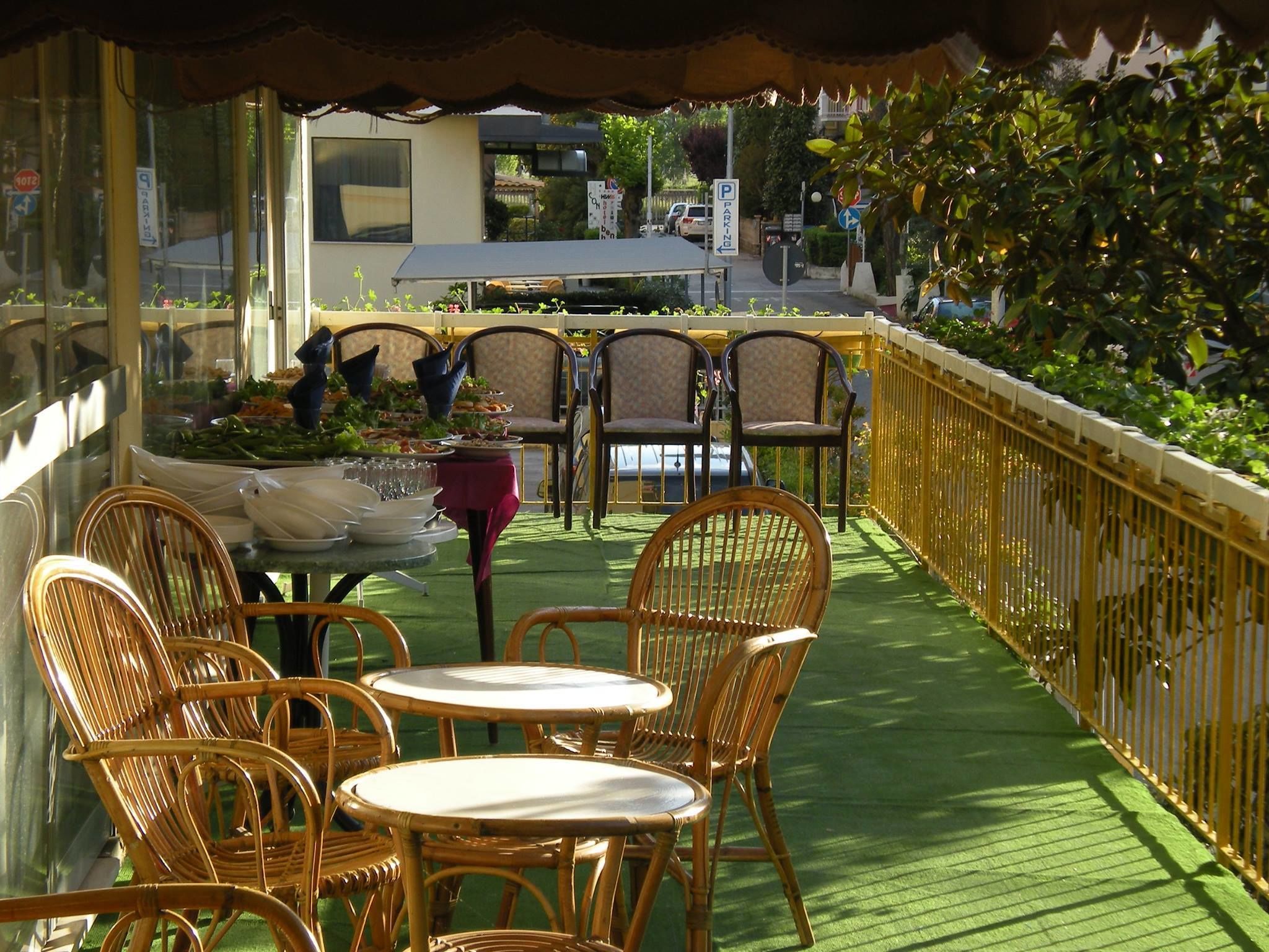 An outdoor patio with wicker chairs and tables, a green artificial turf floor, and a yellow fence.